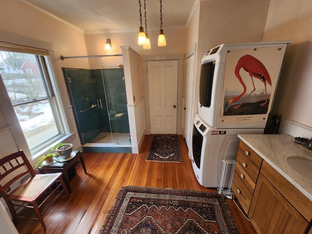 interior space with a shower stall, stacked washing maching and dryer, crown molding, and hardwood / wood-style flooring