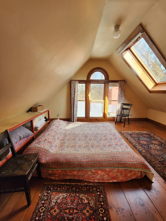 unfurnished bedroom with baseboards, lofted ceiling with skylight, and hardwood / wood-style floors