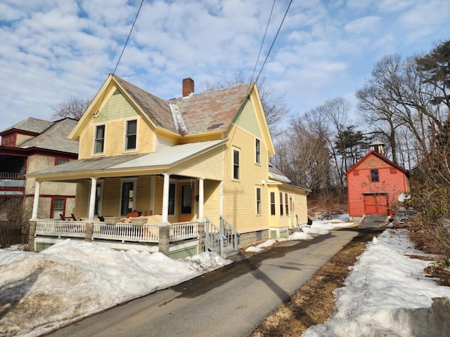 view of front facade featuring an outbuilding, a porch, and a chimney