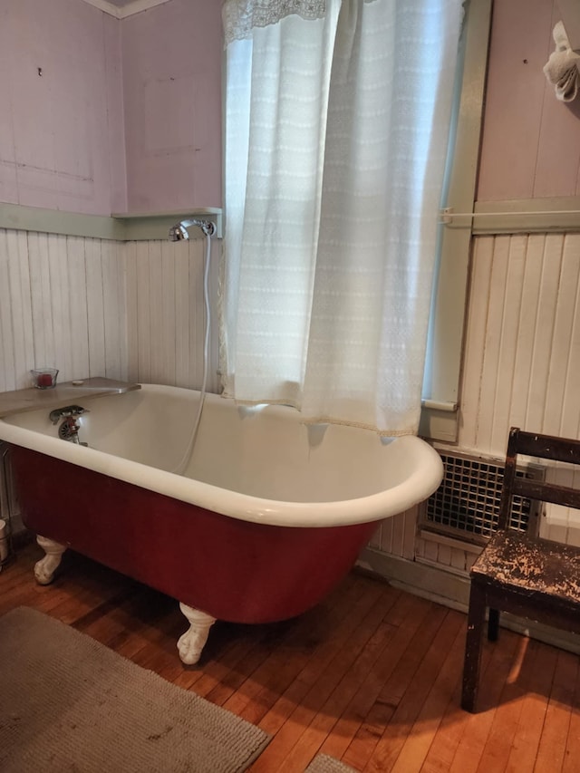 bathroom with a soaking tub, wooden walls, and hardwood / wood-style flooring