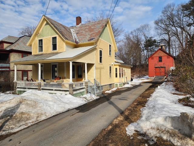 view of front of house featuring an outbuilding, a porch, and a chimney