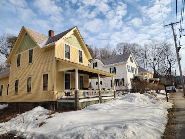 view of snowy exterior featuring a porch and a chimney