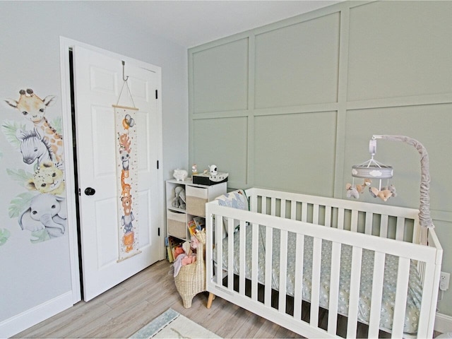 bedroom with a decorative wall, a crib, and light wood-type flooring