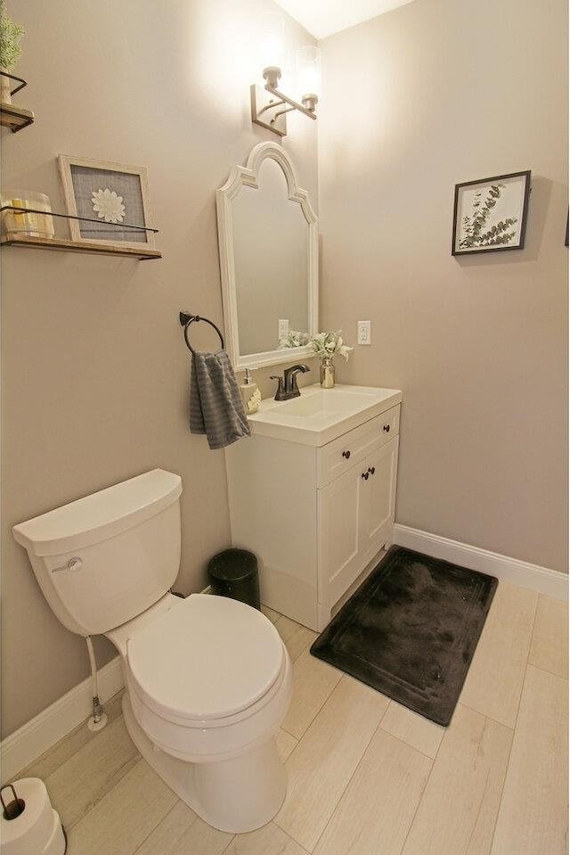 half bathroom featuring baseboards, toilet, and vanity