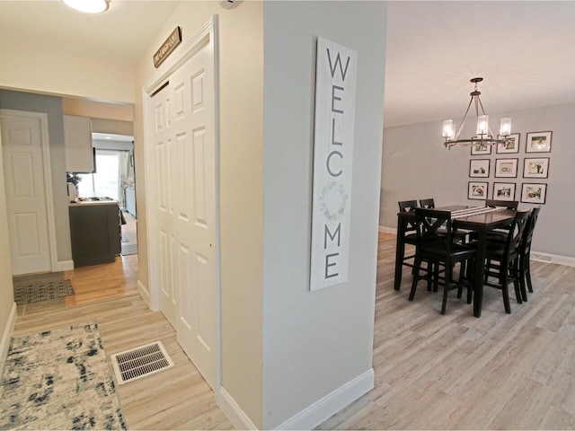 corridor with visible vents, light wood-style flooring, an inviting chandelier, and baseboards