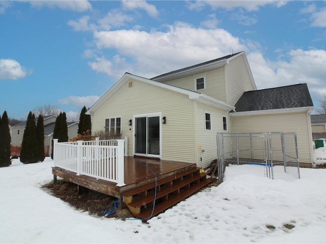 snow covered back of property with a garage and a deck