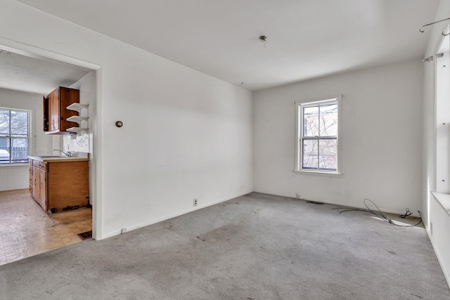 unfurnished room featuring a sink, plenty of natural light, and light colored carpet