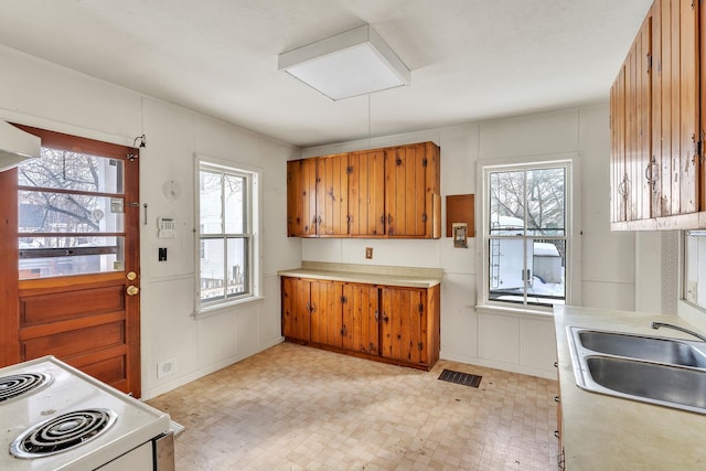 kitchen with visible vents, white range with electric cooktop, light countertops, brown cabinetry, and a sink