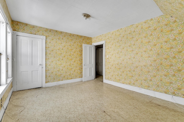 empty room featuring baseboards and wallpapered walls