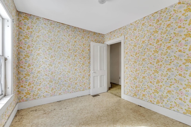 unfurnished room with wallpapered walls, visible vents, and baseboards