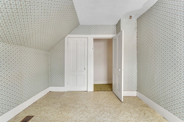 additional living space with visible vents, wallpapered walls, baseboards, and vaulted ceiling