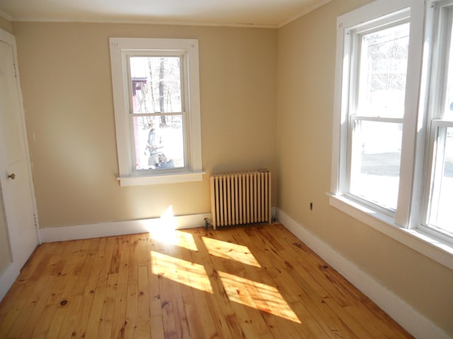 empty room with baseboards, a healthy amount of sunlight, radiator heating unit, and light wood finished floors