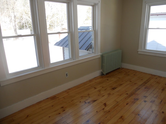 spare room featuring light wood-type flooring, baseboards, a healthy amount of sunlight, and radiator heating unit