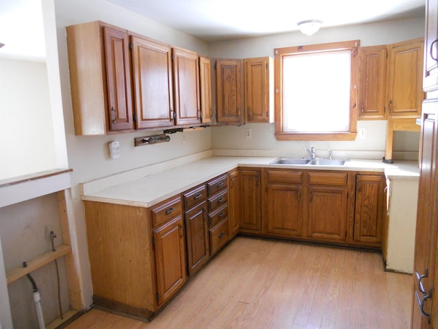 kitchen with light wood finished floors, brown cabinetry, and a sink