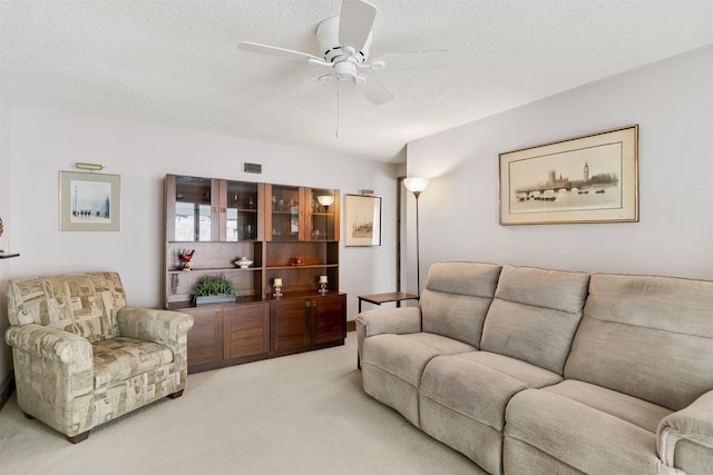 living room featuring a ceiling fan, light colored carpet, visible vents, and a textured ceiling