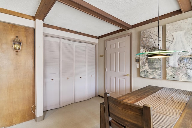 bedroom featuring a closet, beamed ceiling, light colored carpet, and a textured ceiling