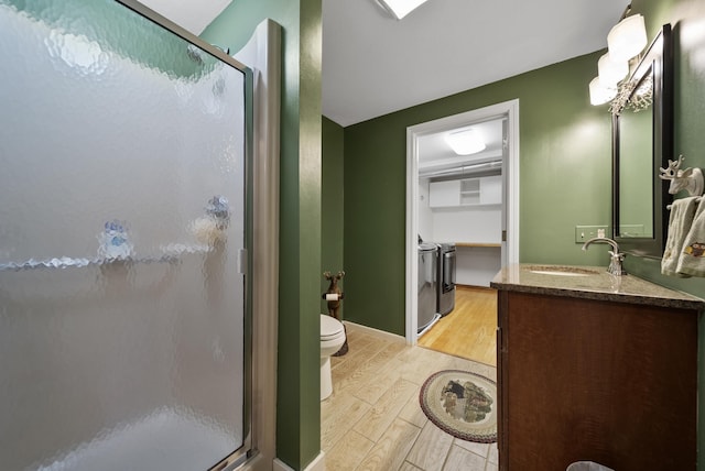 full bath with toilet, a stall shower, washer and dryer, wood finished floors, and vanity