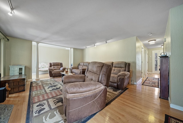 living area with decorative columns, baseboards, wood finished floors, and track lighting