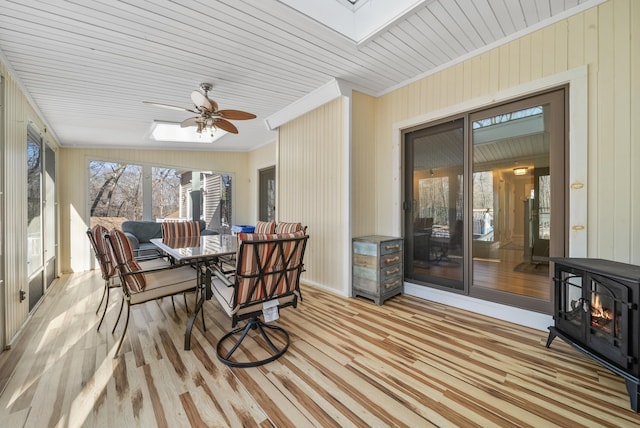 sunroom featuring a wood stove, a skylight, and a ceiling fan