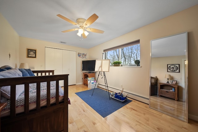 bedroom with visible vents, baseboard heating, light wood-style floors, a closet, and a ceiling fan