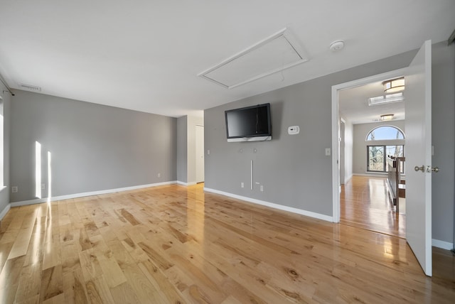 unfurnished living room with light wood-type flooring, visible vents, baseboards, and attic access