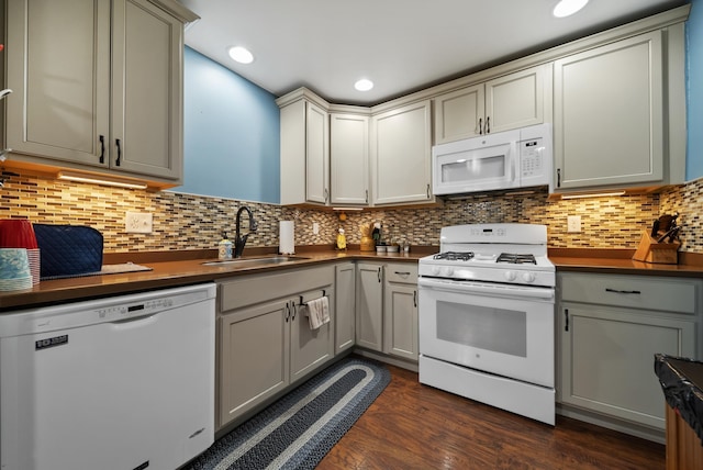 kitchen with a sink, white appliances, dark countertops, and dark wood-style flooring