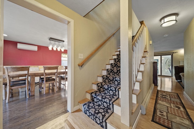 stairway featuring a wall mounted air conditioner, a baseboard heating unit, baseboards, and wood finished floors