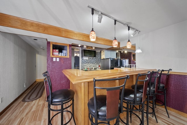 bar with decorative light fixtures, wood finished floors, freestanding refrigerator, black microwave, and bar