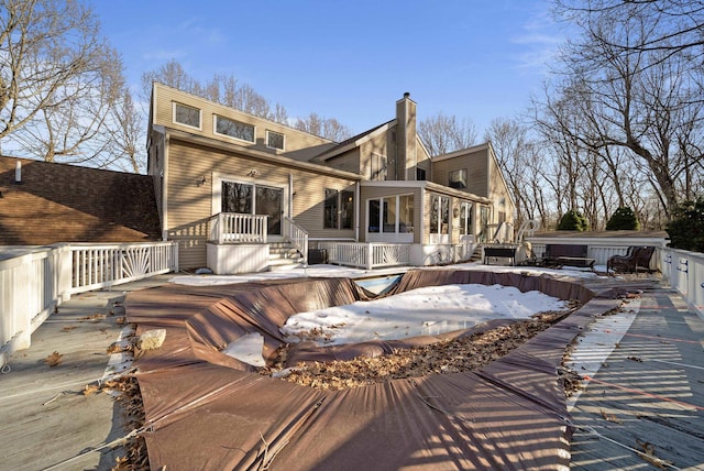 rear view of property with a chimney, a deck, and a sunroom