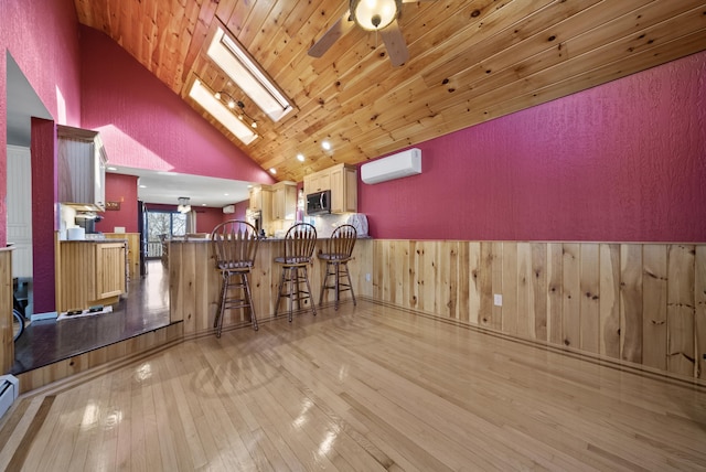 unfurnished dining area with a wainscoted wall, an AC wall unit, light wood-style floors, a skylight, and wood ceiling