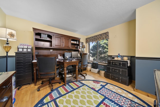 home office featuring wainscoting, a textured ceiling, and light wood-type flooring