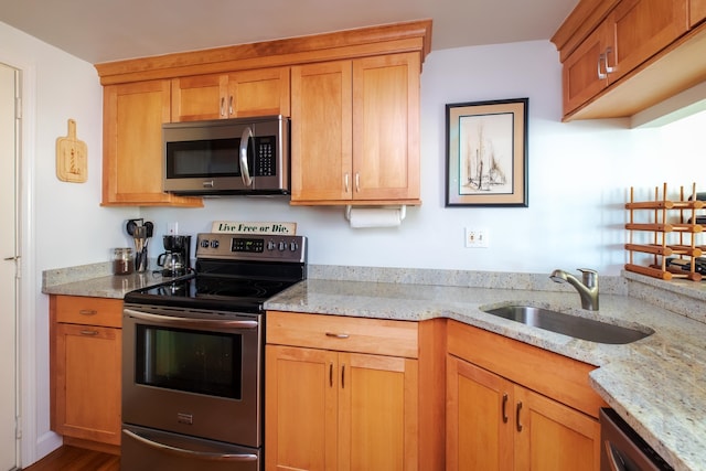 kitchen with light stone counters, appliances with stainless steel finishes, brown cabinetry, and a sink