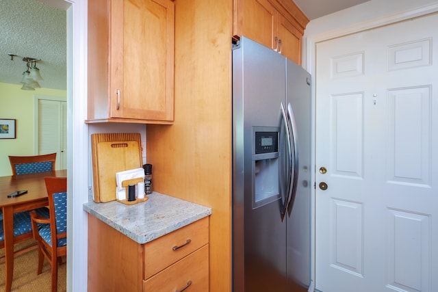 kitchen with light stone counters, track lighting, a textured ceiling, and stainless steel fridge with ice dispenser