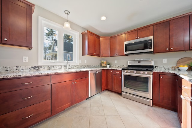 kitchen featuring light stone counters, light tile patterned floors, a sink, appliances with stainless steel finishes, and pendant lighting