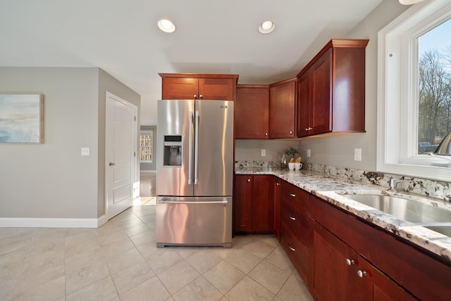 kitchen with baseboards, light stone countertops, stainless steel fridge with ice dispenser, recessed lighting, and a sink