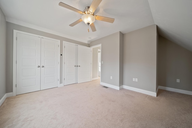 unfurnished bedroom with baseboards, multiple closets, carpet, and vaulted ceiling