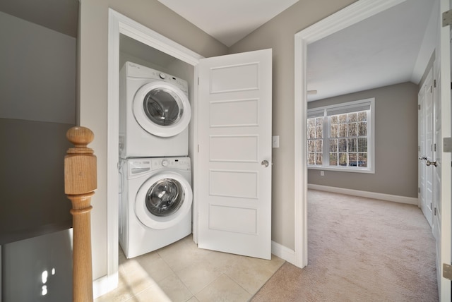 clothes washing area featuring stacked washer / dryer, baseboards, light carpet, laundry area, and light tile patterned floors