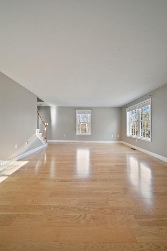 unfurnished living room featuring stairway, plenty of natural light, and light wood finished floors