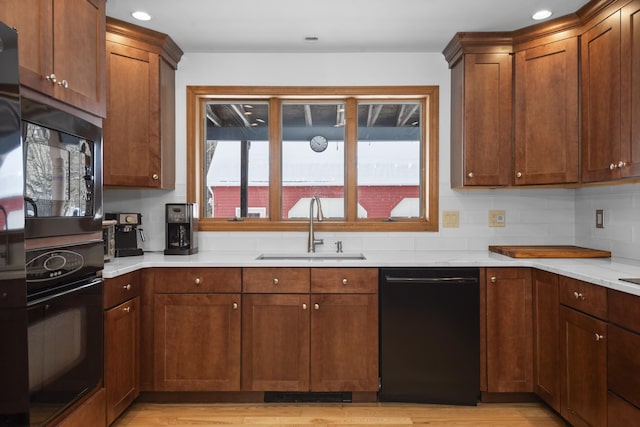 kitchen with a sink, black appliances, light countertops, light wood-type flooring, and backsplash