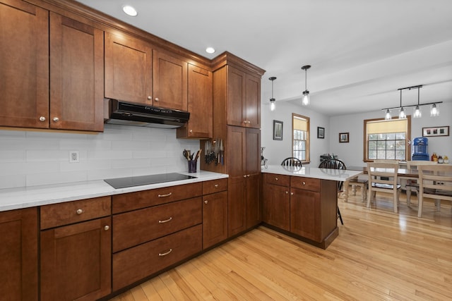 kitchen with a peninsula, black electric cooktop, light countertops, and under cabinet range hood