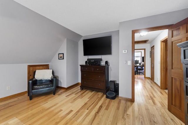 sitting room featuring light wood-style flooring, baseboards, and vaulted ceiling