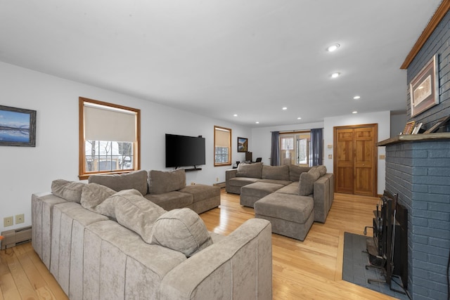 living area with a baseboard heating unit, a brick fireplace, recessed lighting, and light wood finished floors