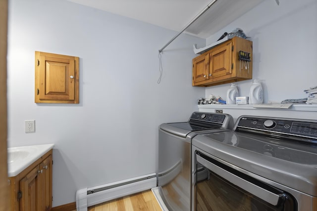 clothes washing area featuring light wood-type flooring, baseboard heating, separate washer and dryer, cabinet space, and a sink