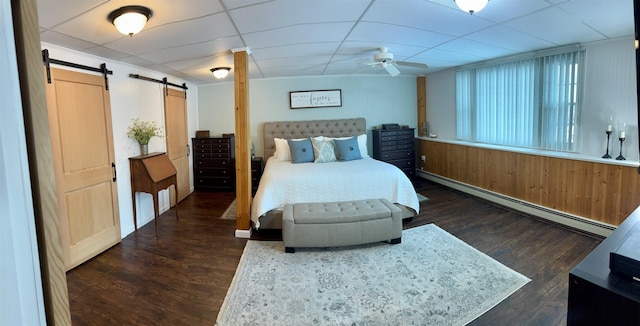 bedroom featuring a drop ceiling, a baseboard heating unit, a barn door, and wood finished floors