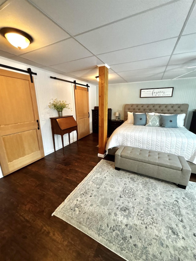 bedroom with a drop ceiling, a barn door, and wood finished floors