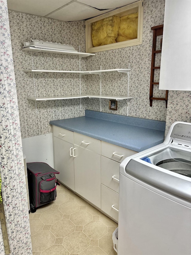 clothes washing area featuring light tile patterned floors, cabinet space, washer / dryer, and wallpapered walls