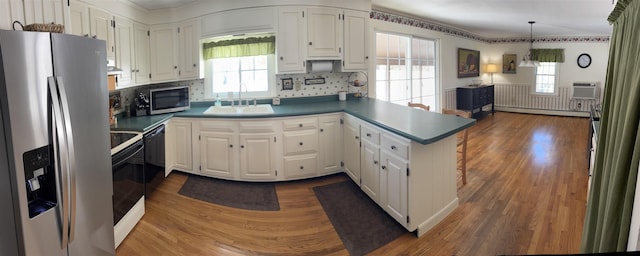 kitchen featuring a sink, appliances with stainless steel finishes, a peninsula, white cabinets, and baseboard heating