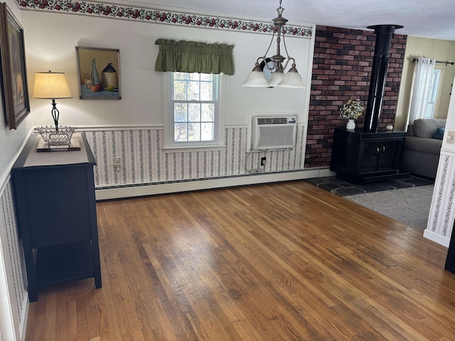 living room featuring a wall mounted AC, a wood stove, wood finished floors, and a baseboard radiator