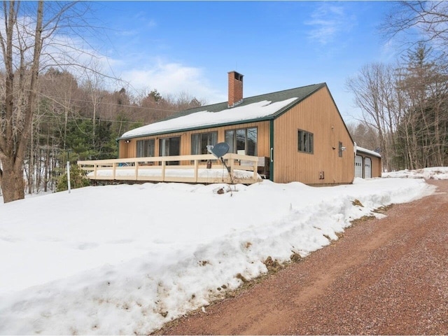 snow covered house featuring a wooden deck and a chimney