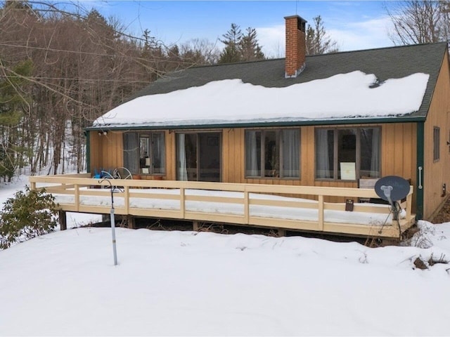 snow covered house with a wooden deck and a chimney